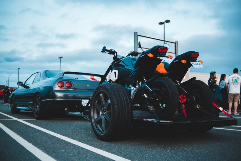 Voiture tractant une remorque porte-moto chargée de deux motos sanglées, prête pour un départ en vacances.